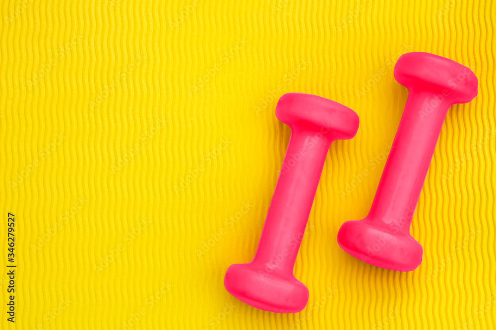 Pink dumbbells on the background of a yellow yoga mat. The concept of a sports lifestyle, weight loss, exercise, energy, charging emotions. Top view. Copy space. Pink dumbbells on the background of a yellow yoga mat. The concept of a sports lifestyle, weight loss, exercise, energy, charging emotions. Top view. Copy space.