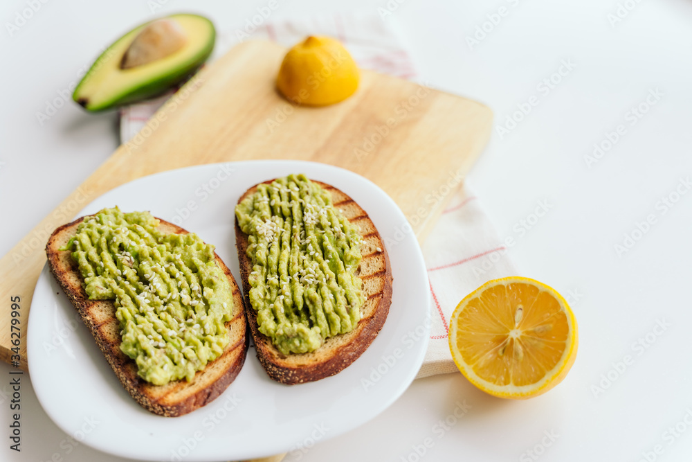 toasted bread with avocado paste. Avocado mixed with lemon juice is spread on bread. toast with avocado lies on a white plate and wooden cutting board. health food concept, vegan, vegetarian