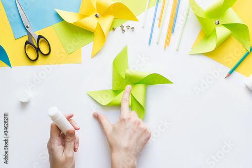 How to make paper green windmill toy with children at home. Step by step instructions. Hands making DIY summer project. Top view. Step 8. Glue remaining corners, overlaying each other.