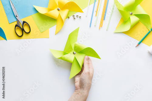 How to make paper green windmill toy with children at home. Step by step instructions. Hands making DIY summer project. Top view. Step 10. Attach office button to mark center. photo