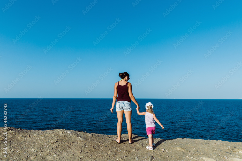 mother and daughter look at the sea from the shore