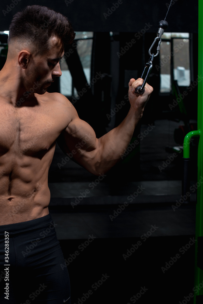 male athlete shows near the green simulator how to perform the exercise for the deltoid and biceps and triceps muscles in the gym, sexy guy bodybuilder, sports lifestyle, home sports.