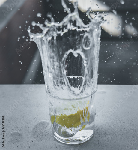fotografía de un limón cayendo sobre un baso de agua. El agua salpica al entorno generando figuras en el aire. Imagen refrescante. 