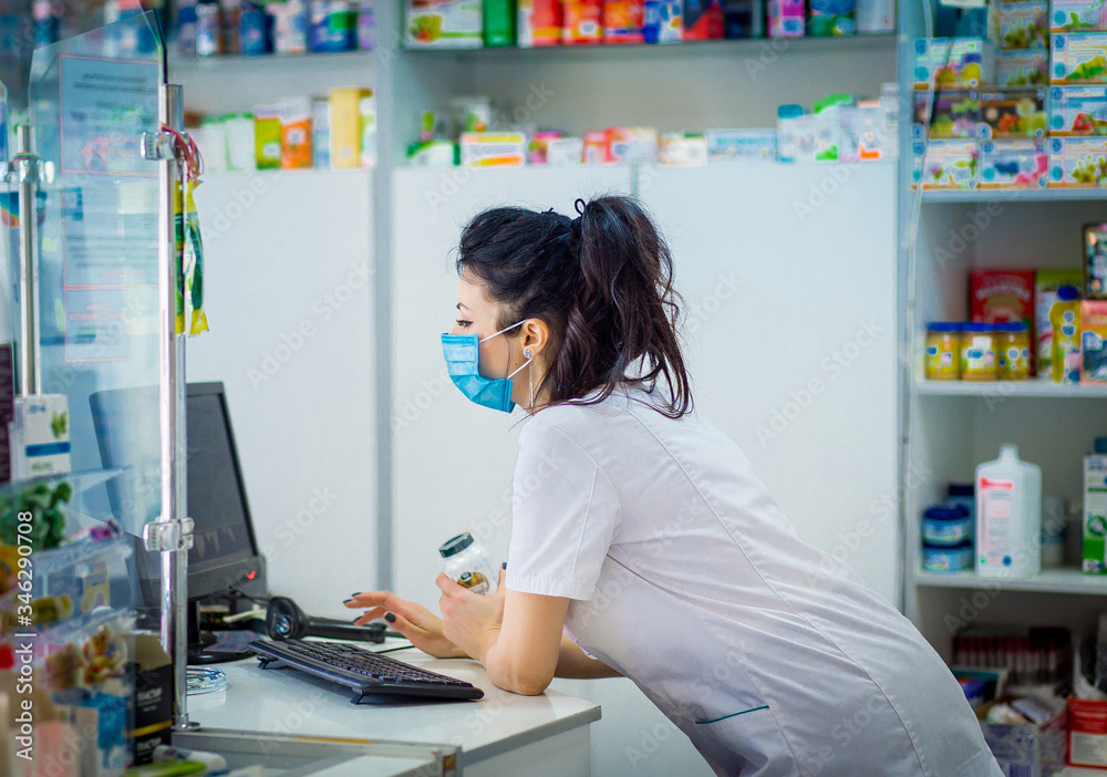 the pharmacist is holding a container with medicine and is studying it. A pharmacist in a medical mask on his face punches medicine in a computer. the pharmacist is holding a container with medicine and is studying it. A pharmacist in a medical mask on his face punches medicine in a computer.