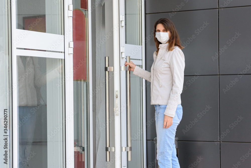 girl in a medical mask near the entrance to the room holds the door handle