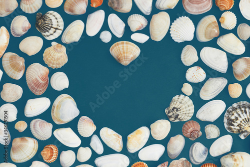 The heart made with the seashells on the dark teal paper background. Copy space. Flat lay, top view. Abstract. World ocean day.