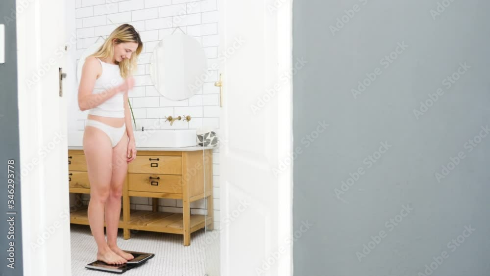 Woman stepping on the weight scale happy with her weight loss result Woman stepping on the weight scale happy with her weight loss result