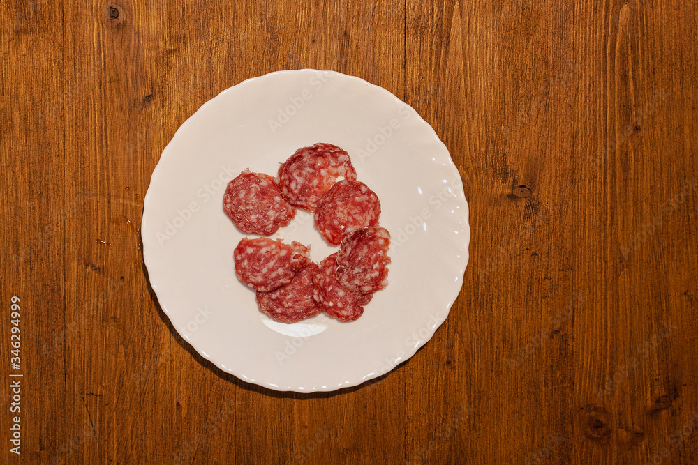 Top view of plate with salami slices on wooden background. Concept: cooking, meat, restaurant Top view of plate with salami slices on wooden background. Concept: cooking, meat, restaurant