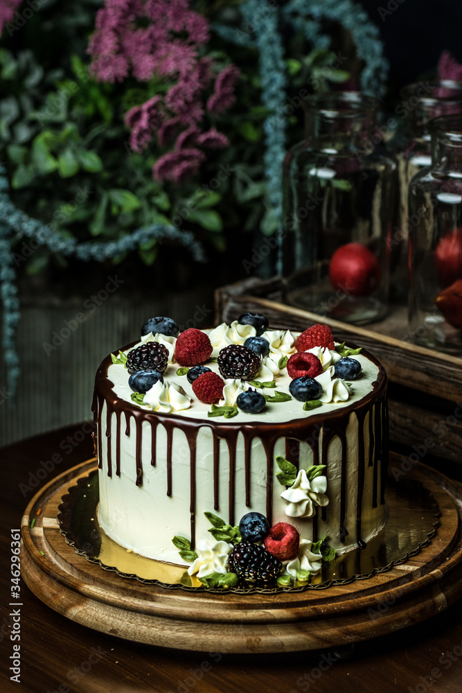 Beautiful white cake .Decorate with fruits-strawberries, raspberries, blackberries,blueberries, chocolate.Handmade work.White porcelain high stand