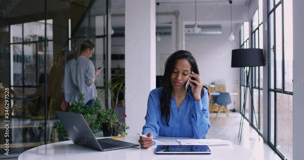 Tired dark skinned female employee talking on mobile phone via call and checking information with digital tablet while her coworking employee walking on background, Slow motion effect on 4K RED camera