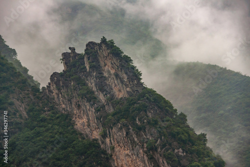 Baidicheng, China - May 7, 2010: Qutang Gorge on Yangtze River. Landscape of gray cloudscape descends in waves along slopes of green covered mountains, one beigh sharp topped.