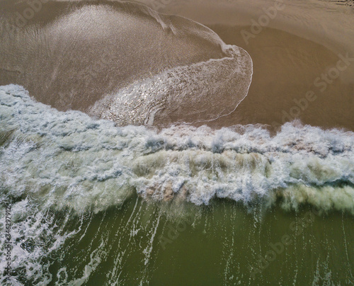 Aerial drone image of foamy waves washing up on the beautiful sandy beach of Island Beach State Park in New Jersey creating colorful abstract images