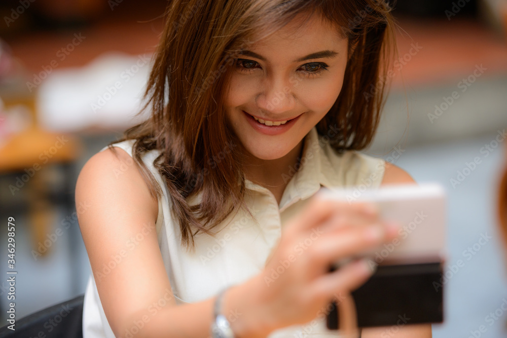 Face of happy young beautiful Asian woman taking selfie at restaurant