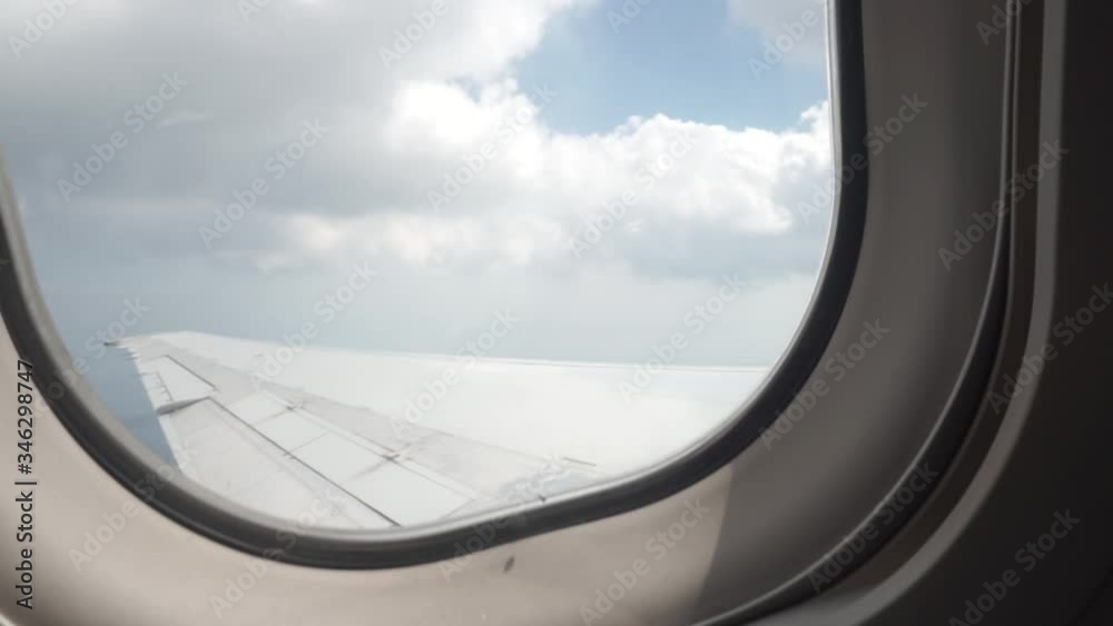 A plane in the air flies wing under the clouds in the blue sky. Shooting through the window of the illuminator A plane in the air flies wing under the clouds in the blue sky. Shooting through the window of the illuminator