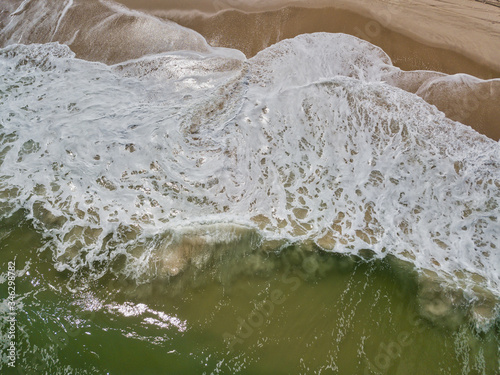Aerial drone image of foamy waves washing up on the beautiful sandy beach of Island Beach State Park in New Jersey creating colorful abstract images