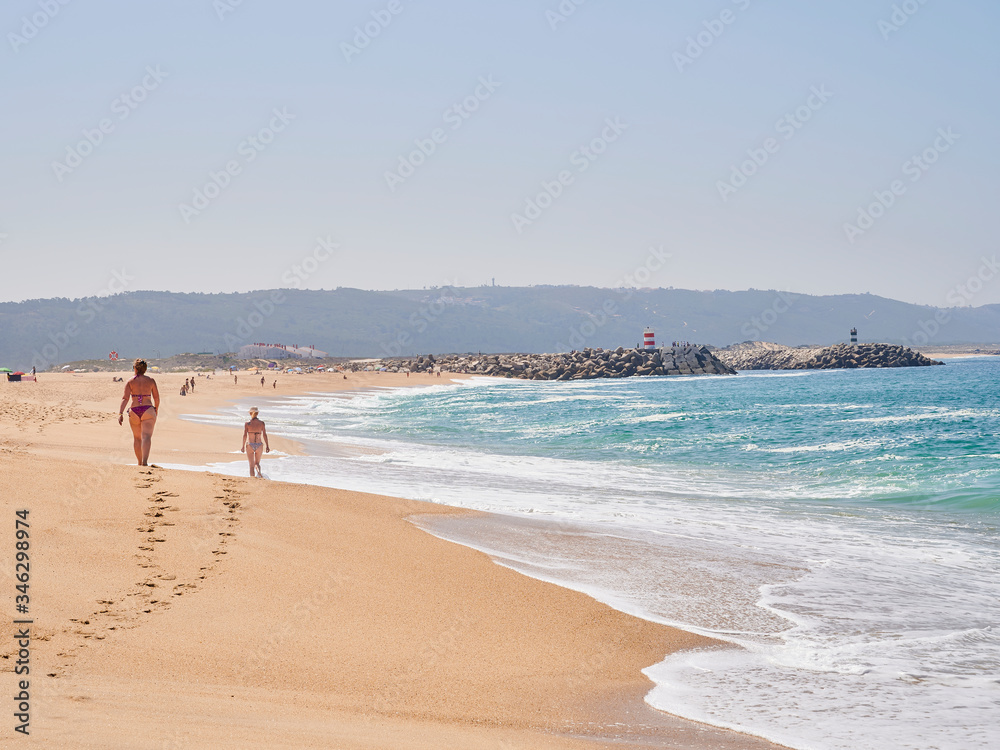 SWOmans walking on summer morning at beach of Nazaré in Portugal