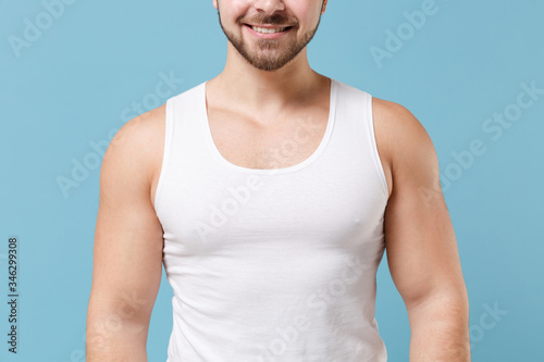 Fotografi Cropped image of strong smiling young bearded guy 20s in white singlet posing isolated on pastel blue wall background studio portrait