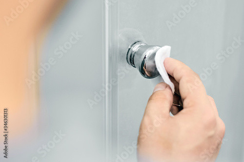 Close-up of a person who processes and disinfects the door handle with alcohol at home and in the office. Concept of prevention, protection and hygiene against virus and bacteria