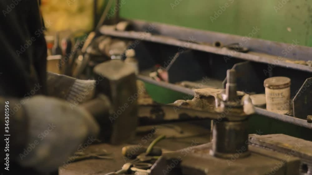 Asian in gloves and work clothes is repairing a spare part of a car in a garage, closeup. Asian in gloves and work clothes is repairing a spare part of a car in a garage, closeup.