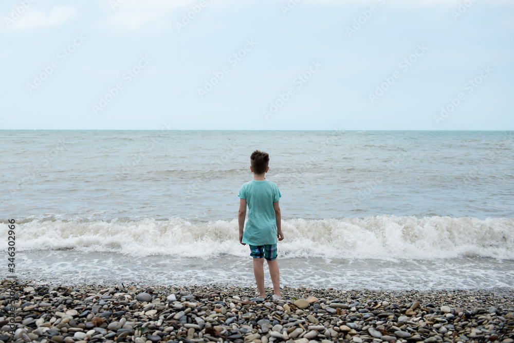 a blond boy in a green t-shirt on the beach. Light waves on the sea.