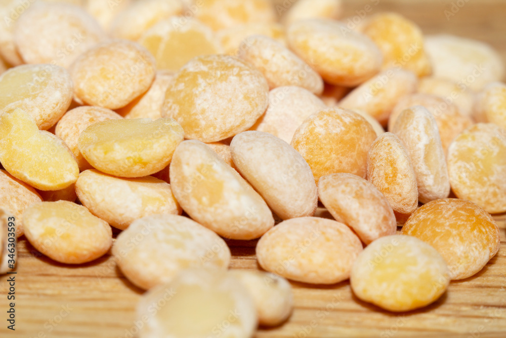 Raw split peas of yellow variety on the wooden surface and scattered beside, close-up in selective focus. Vegan food, stock photo Raw split peas of yellow variety on the wooden surface and scattered beside, close-up in selective focus. Vegan food, stock photo