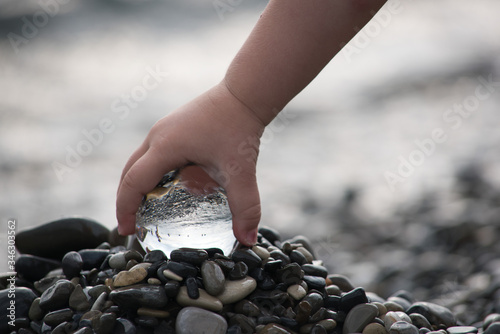 a child's hand holds a glass ball against the background of the sea