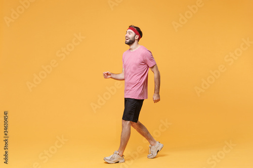Side view of cheerful young bearded fitness sporty guy sportsman in headband t-shirt spend weekend in home gym isolated on yellow background. Workout sport motivation lifestyle concept. Looking aside.