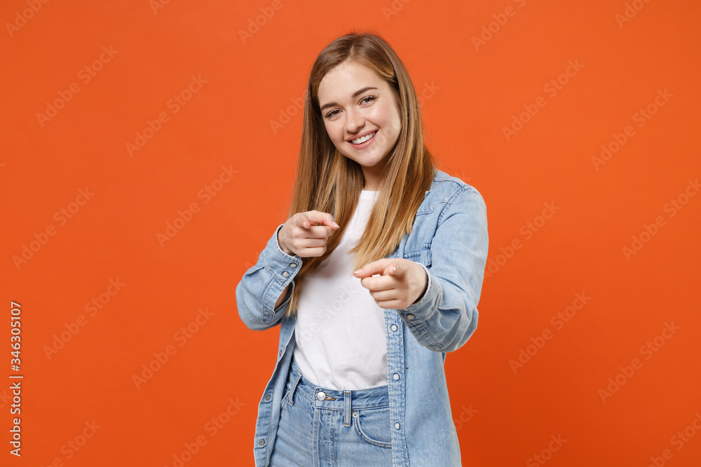 Smiling young woman girl in casual denim clothes posing isolated on orange background studio portrait. People sincere emotions lifestyle concept. Mock up copy space. Pointing index fingers on camera. Smiling young woman girl in casual denim clothes posing isolated on orange background studio portrait. People sincere emotions lifestyle concept. Mock up copy space. Pointing index fingers on camera.