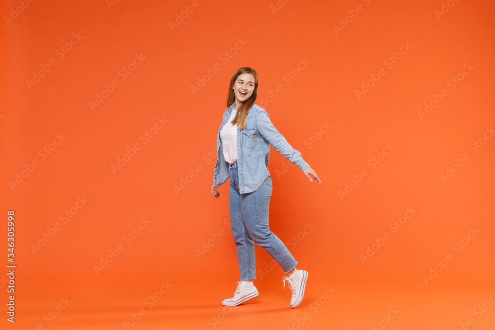 Side view of funny young woman girl in casual denim clothes posing isolated on orange background studio portrait. People emotions lifestyle concept. Mock up copy space. Looking aside, spreading hands. Side view of funny young woman girl in casual denim clothes posing isolated on orange background studio portrait. People emotions lifestyle concept. Mock up copy space. Looking aside, spreading hands.