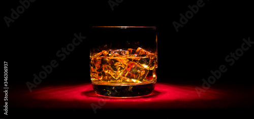 A glass of whiskey on the rocks on the red table in the middle
