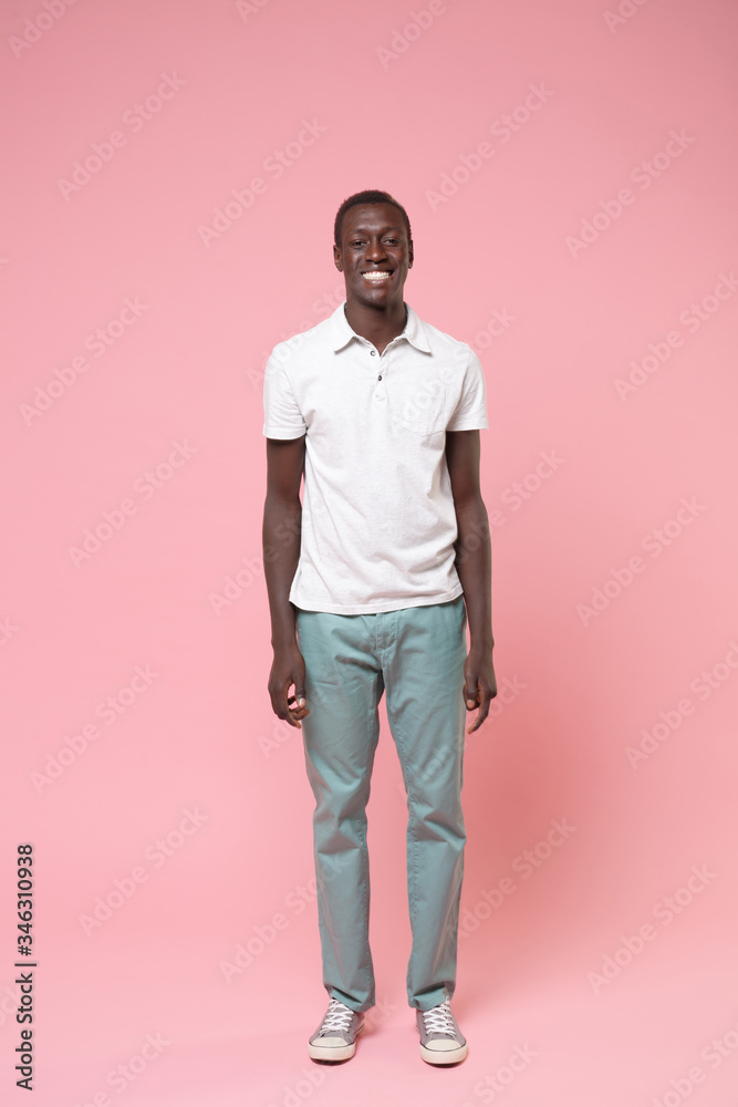 Smiling young african american man guy in white polo shirt, turquoise trousers posing isolated on pastel pink wall background in studio. People lifestyle concept. Mock up copy space. Looking camera.