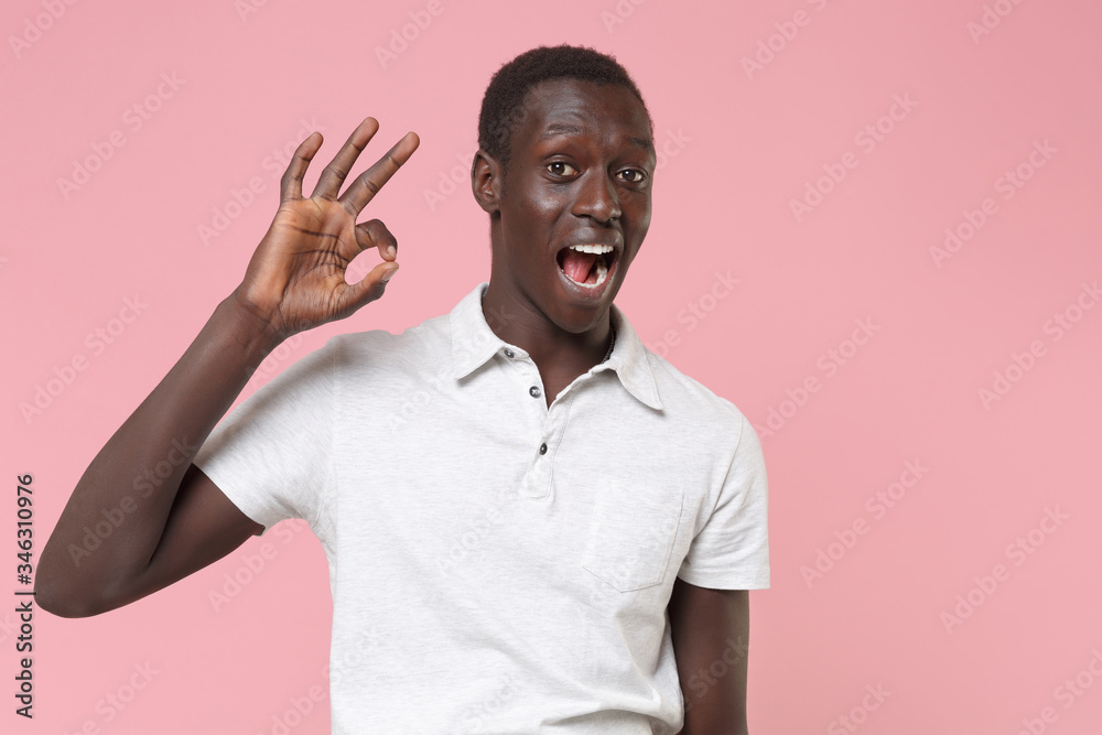 Excited young african american man guy in white polo shirt posing isolated on pastel pink background studio portrait. People sincere emotions lifestyle concept. Mock up copy space. Showing OK gesture. Excited young african american man guy in white polo shirt posing isolated on pastel pink background studio portrait. People sincere emotions lifestyle concept. Mock up copy space. Showing OK gesture.