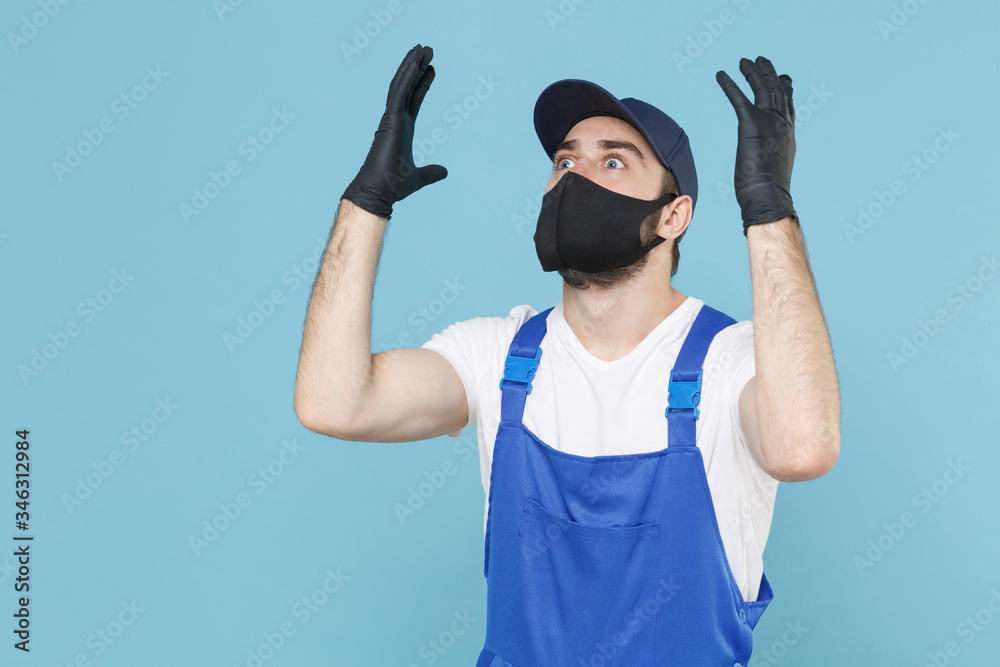 Fototapeta premium Delivery man in cap t-shirt coveralls uniform sterile face mask gloves isolated on blue background studio. Guy employee courier Service quarantine pandemic coronavirus virus covid-19 2019-ncov concept