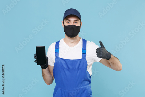 Delivery man in cap t-shirt uniform sterile mask gloves isolated on blue background studio. Guy employee courier hold mobile cell phone Service quarantine coronavirus virus covid-19 2019-ncov concept.