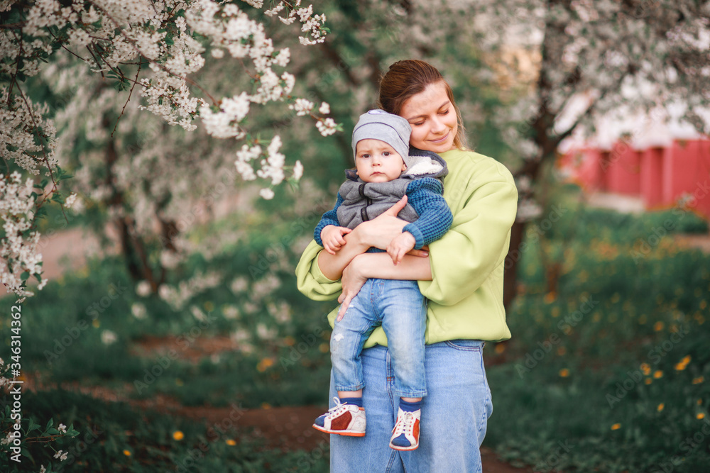 A mother plays and talks with a child against the background of a flowering tree A mother plays and talks with a child against the background of a flowering tree