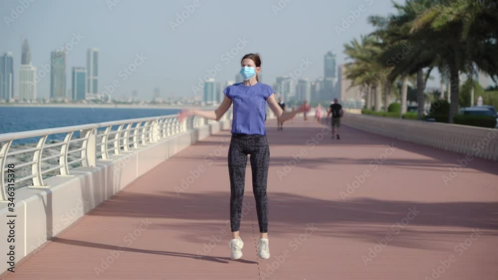 girl does exercise jumping-jack in medicine mask. background sea and buildings.covid 19. antivirus measures. quarantine time girl does exercise jumping-jack in medicine mask. background sea and buildings.covid 19. antivirus measures. quarantine time