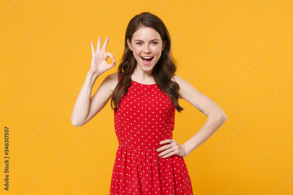 Excited young brunette woman girl in red summer dress posing isolated on yellow wall background studio portrait. People sincere emotions lifestyle concept. Mock up copy space. Showing OK gesture. Excited young brunette woman girl in red summer dress posing isolated on yellow wall background studio portrait. People sincere emotions lifestyle concept. Mock up copy space. Showing OK gesture.