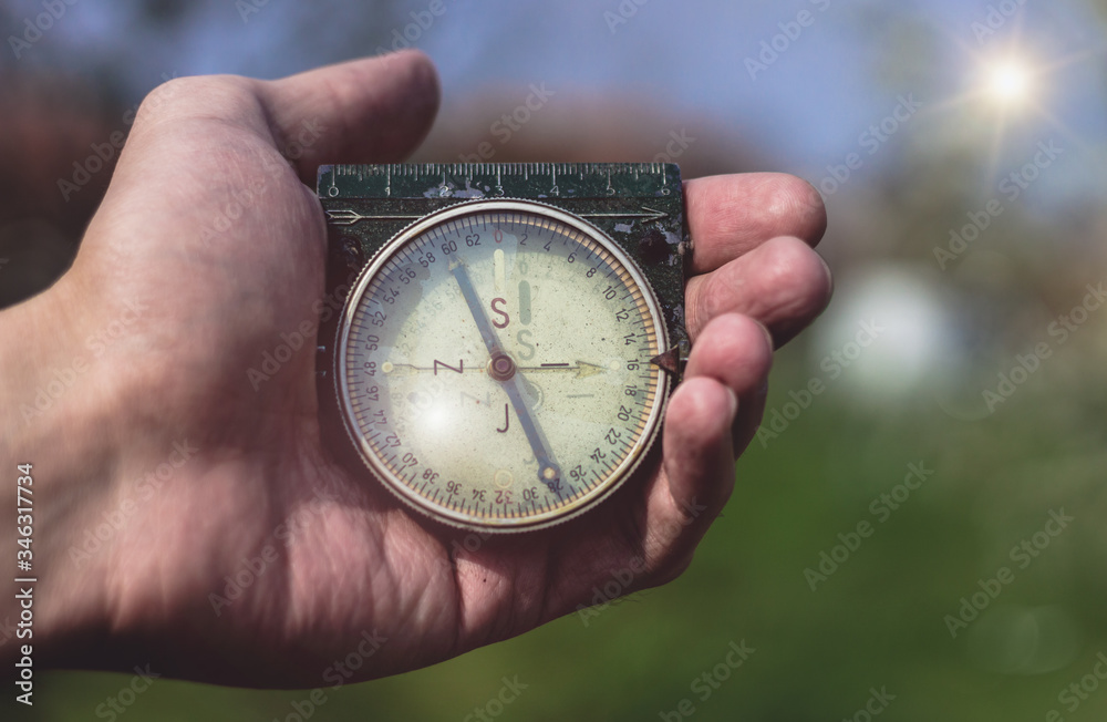 Man holding an old compass in one hand. Male holding a military compass showing direction. Blue sky and sun in the background, first person point of view, close up. Man holding an old compass in one hand. Male holding a military compass showing direction. Blue sky and sun in the background, first person point of view, close up.