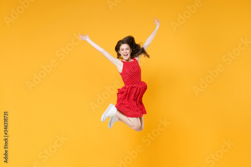Cheerful young brunette woman girl in red summer dress posing isolated on yellow background studio portrait. People sincere emotions lifestyle concept. Mock up copy space. Jumping, spreading hands.