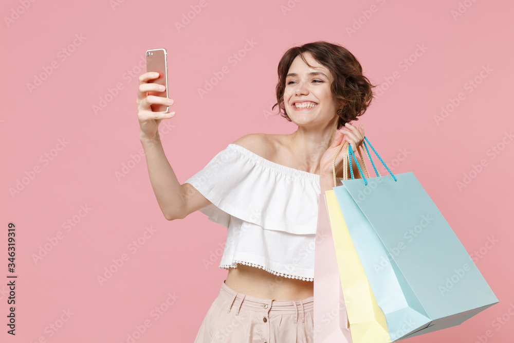 Smiling young woman girl in summer clothes hold package bag with purchases isolated on pink background in studio. Shopping discount sale concept. Mock up copy space. Doing selfie shot on mobile phone. Smiling young woman girl in summer clothes hold package bag with purchases isolated on pink background in studio. Shopping discount sale concept. Mock up copy space. Doing selfie shot on mobile phone.