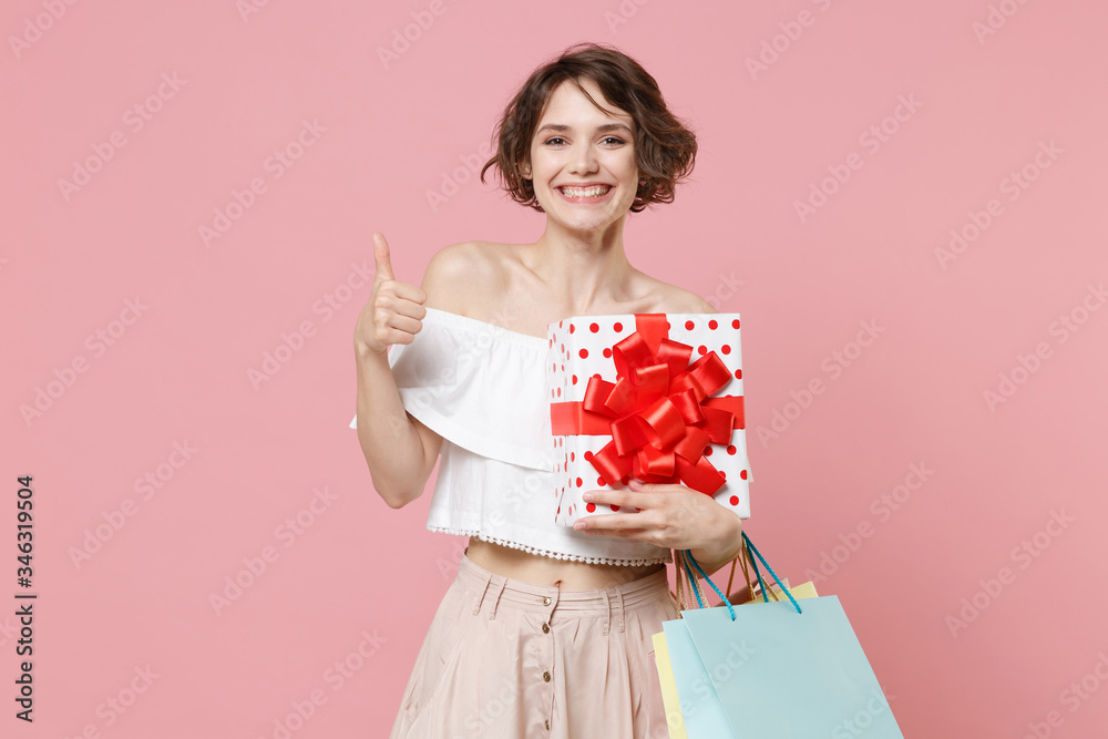 Smiling woman in summer clothes isolated on pink background. Shopping discount sale concept. Mock up copy space. Hold package bag with purchases red present box with gift ribbon bow showing thumb up. Smiling woman in summer clothes isolated on pink background. Shopping discount sale concept. Mock up copy space. Hold package bag with purchases red present box with gift ribbon bow showing thumb up.