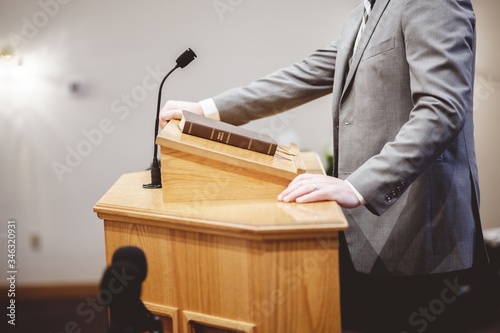 Selective focus shot of a male standing and speaking from the pulpit photo