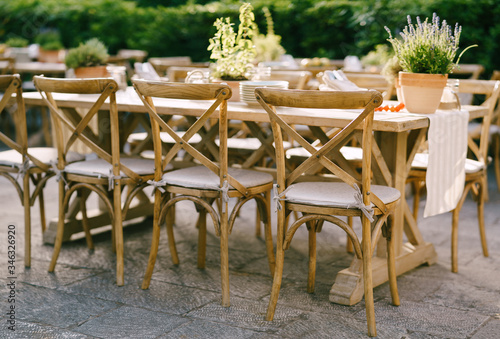 Wedding dinner table reception. Ancient wooden chairs near a large heavy wooden table with a rag runner and a pot of flowering lavender, on the stone floor. Open-air banquet, outside