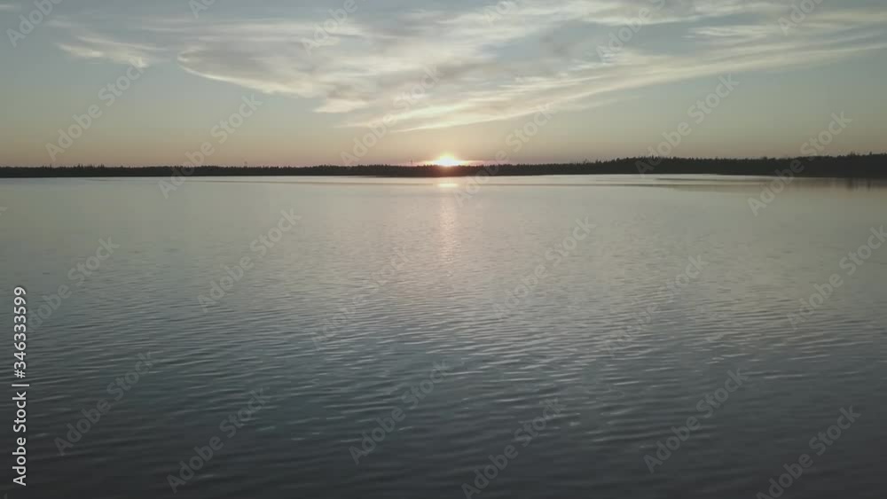 Flight over the expanse of water. Sunset on the lake. Reflection of clouds on the sky in the calm water of a pond. Reflection of the sun in the lake. Flight over the expanse of water. Sunset on the lake. Reflection of clouds on the sky in the calm water of a pond. Reflection of the sun in the lake.