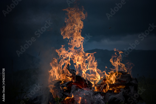 dark scenery of burning fire against defocused mountain silhouette and cloudy sky in the evening on a countryside field