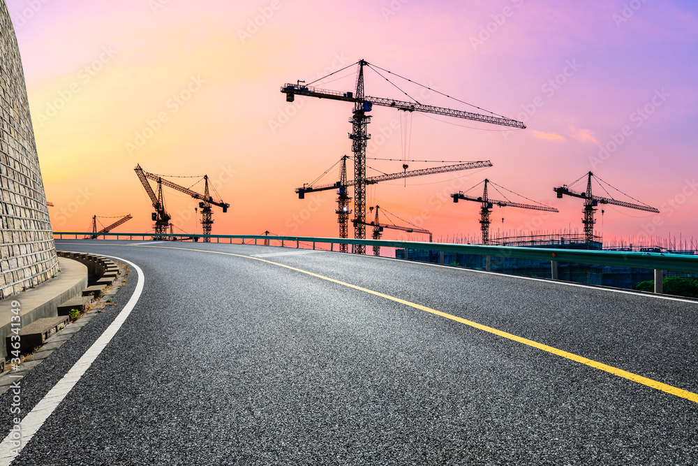 Fototapeta premium Empty asphalt road and construction site landscape at sunrise.