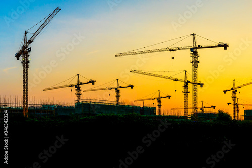 Tower crane and building construction site silhouette at sunrise.