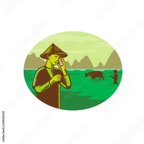 Retro woodcut style illustration of Vietnamese farmer wearing conical hat talking on mobile, cellular phone or cellphone with mountain and rice paddy field in background set inside oval, 