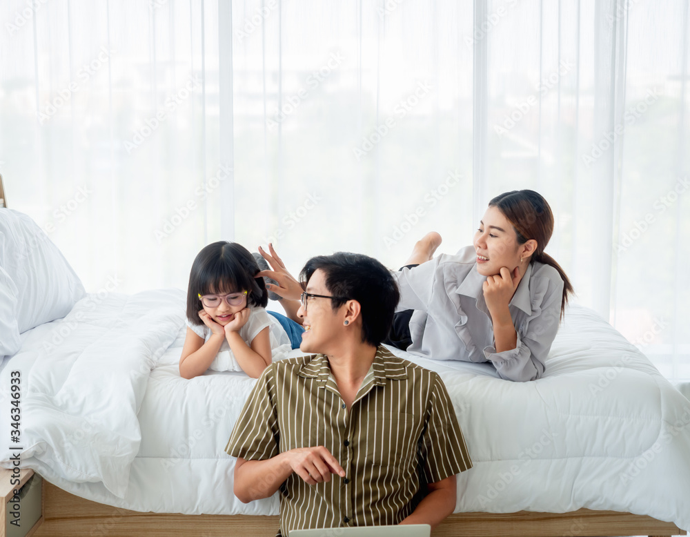 happy family in bed room concept.father siting on floor using laptop notebook mother and daugther lying on bed in bedroom . happy family in bed room concept.father siting on floor using laptop notebook mother and daugther lying on bed in bedroom .