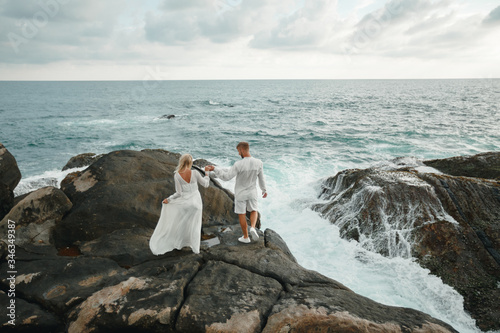 Bride and groom holding hands and walking on a cliff above the sea, romantic moment